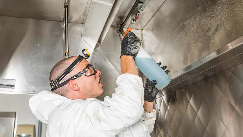 Technician applying degreaser inside a stainless steel commercial kitchen exhaust canopy